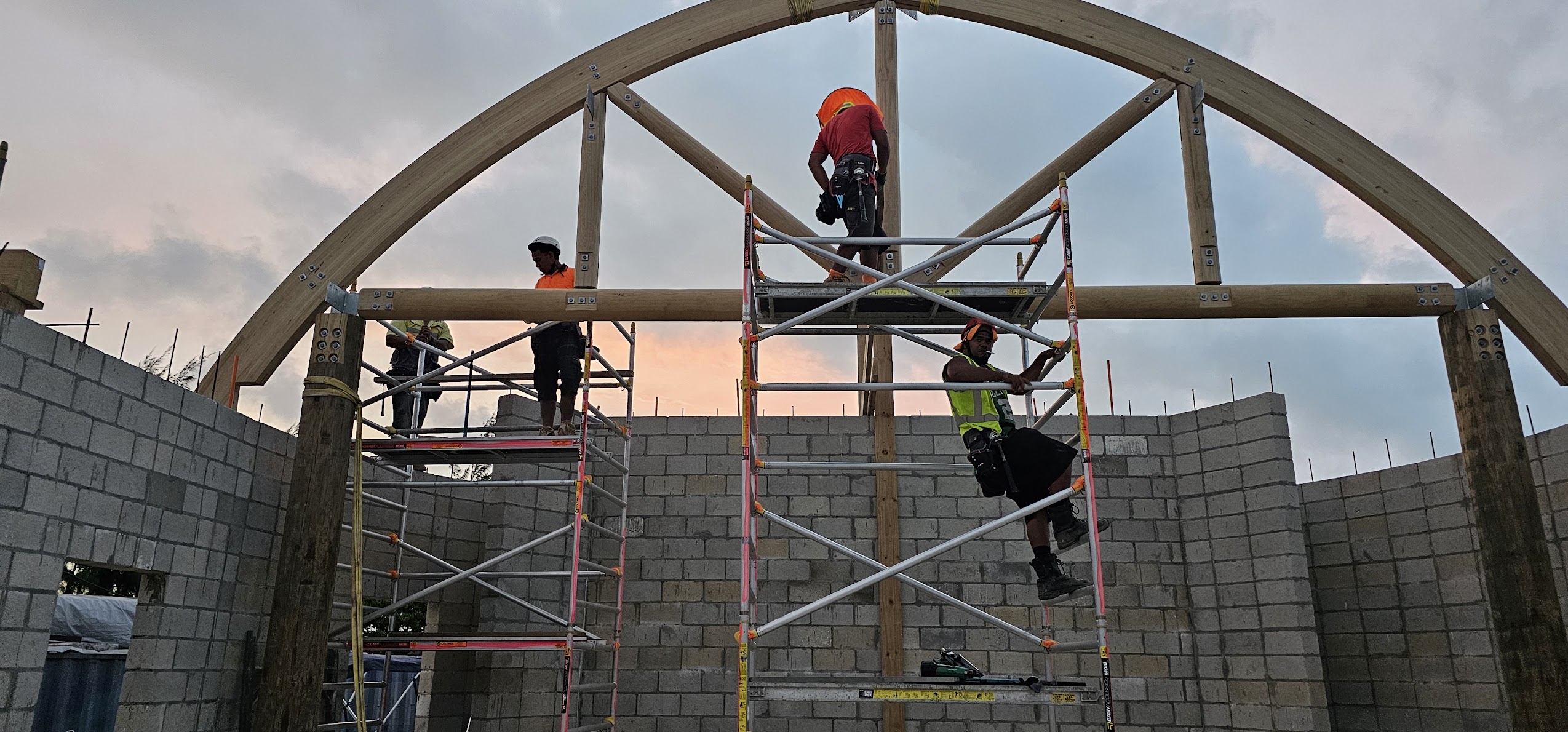 Construction workers installing large curved timber trusses and structural framing on a specialised commercial building project by Build N Concrete Ltd.